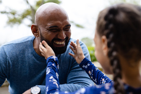 Smiling biracial father with daughter touching beard in garden. Family, love, togetherness, home, lifestyle and domestic life, unaltered.の写真素材