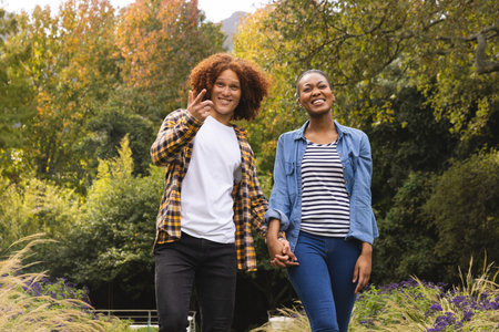 Happy diverse couple holding hands, walking in garden and talking. Togetherness, relationship, free...
