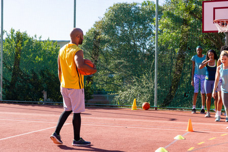 Diverse group of women listening to male coach with basketball at basketball court with cones. Sport, activity, togetherness and lifestyle, unaltered.の写真素材