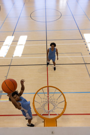 Biracial male basketball players wearing blue sports clothes and shooting basketball at gym. Sport, activity and lifestyle, unaltered, copy space.の写真素材