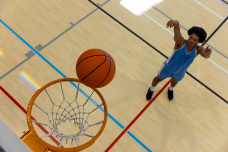 Biracial male basketball player wearing blue sports clothes and shooting basketball at gym. Sport,...