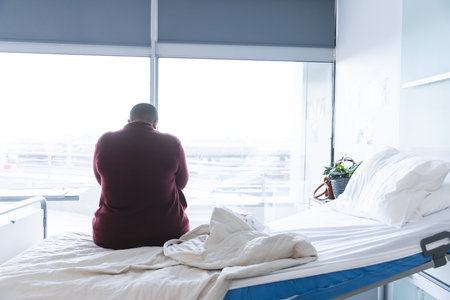African american female patient sitting on bed in patient room at hospital, copy space. Hospital, mental health, medicine and healthcare, unaltered.の写真素材