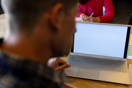 Laptop with copy space on screen and caucasian colleagues working at desk in casual office. Casual...