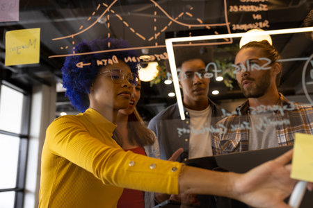 Diverse creative colleagues in discussion brainstorming making notes on glass wall in office. Casual...