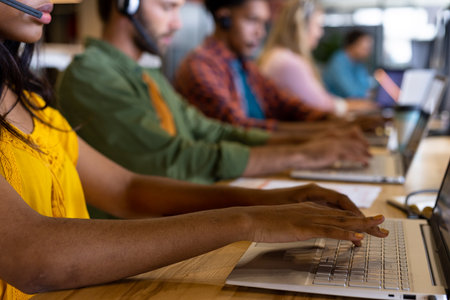 Diverse male and female creative colleagues working using computers and phone headsets in office....