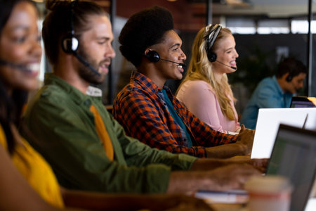 Diverse male and female creative colleagues working using phones headsets and computers in office....