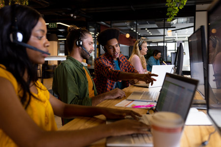 Diverse male and female creative colleagues working using phones headsets and computers in office....