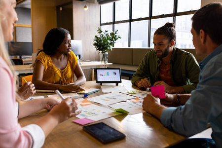 Diverse creative colleagues in discussion brainstorming using tablet and notes at table in office. Casual office, brainstorm, business, teamwork, business and creative work, unaltered.の写真素材