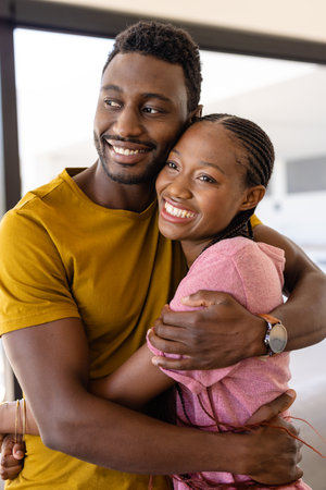 Happy african american couple hugging in living room. Lifestyle, relationship, togetherness and domestic life, unaltered.の写真素材