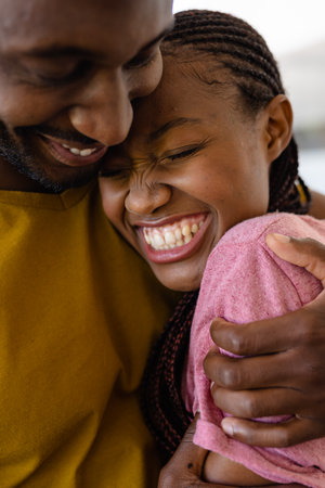 Happy african american couple embracing in living room. Lifestyle, relationship, togetherness and domestic life, unaltered.の写真素材
