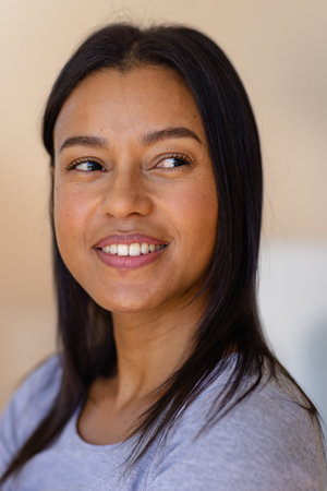 Portrait of happy biracial woman against beige wall at home. Lifestyle and domestic life, unaltered.