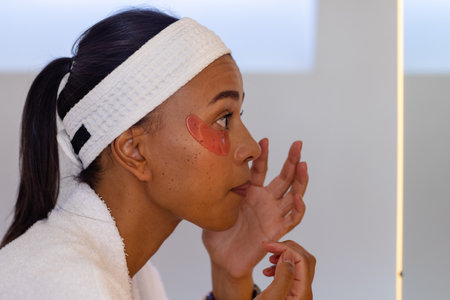 Biracial woman in bathrobe wearing eye mask in bathroom. Lifestyle, beauty, self care, wellbeing and...
