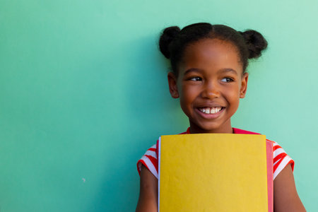 Happy african american schoolgirl holding books at elementary school, copy space. Education, childhood, development, learning and elementary school, unaltered.の写真素材