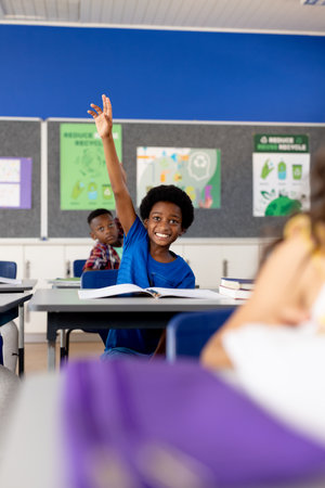 Diverse elementary schoolchildren sitting at desks and raising hands in class. Education, childhood, development, learning and elementary school, unaltered.の写真素材