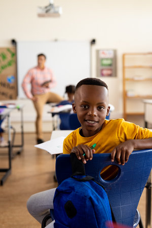 Portrait of happy african american elementary schoolboy sitting at desk in class. Education,...