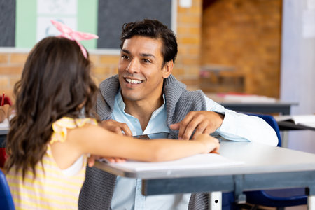 Diverse male teacher using tablet teaching children at desks in elementary school class. School, learning, childhood, communication, teaching and education, unaltered.の写真素材