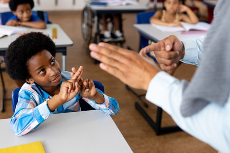 Diverse male teacher teaching school boy using sign language in class at elementary school. School,...