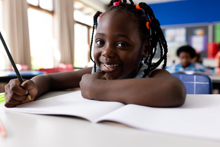 Portrait of african american girl writing in classroom at elementary school. School, learning,...