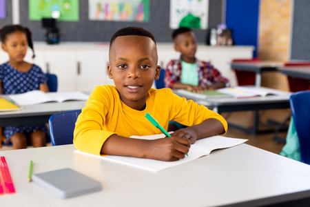 Portrait of happy african american elementary schoolboy sitting at desk in class. School, learning, childhood and education, unaltered.の写真素材