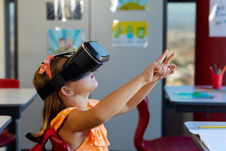 Focused caucasian schoolgirl sitting at desk and using vr headset in classroom at elementary school....