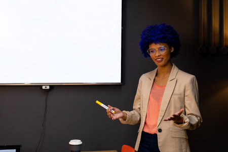 Happy biracial casual businesswoman with blue afro making presentation at whiteboard with copy...