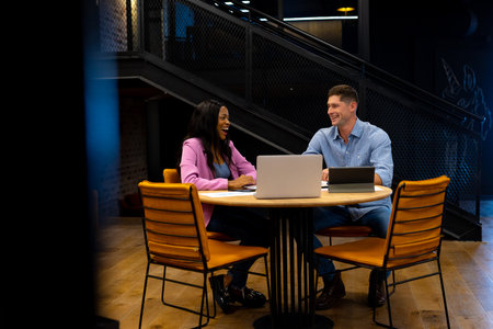 Happy diverse male and female colleague using tablet and laptop in casual office meeting. Casual...