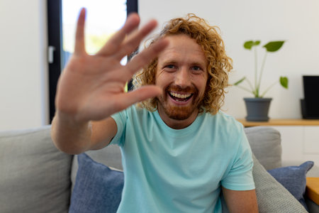 Happy caucasian man sitting on sofa and having video call. Lifestyle, communication and domestic life, unaltered.の写真素材