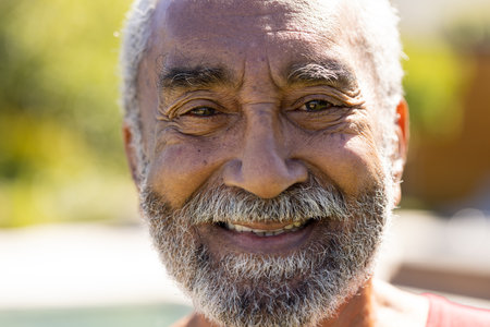Portrait of happy senior biracial man with beard looking at camera and smiling in sunny garden....