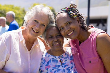 Portrait of happy senior diverse female friends embracing and smiling in garden. Senior lifestyle, friendship and relaxation, retirement, unaltered.の写真素材