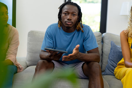 Group of diverse people sitting on sofa, using tablet and talking in group therapy session....