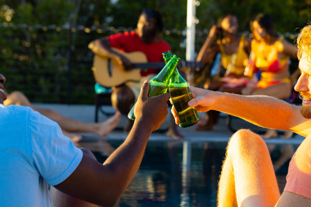 Happy diverse group of friends having pool party, drinking beer and playing guitar in garden....
