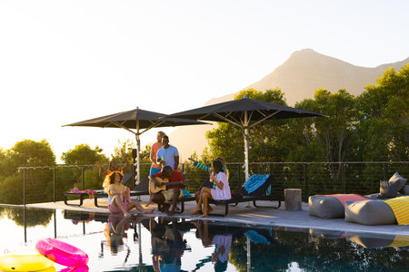 Happy diverse group of friends having pool party and playing guitar in garden, copy space....