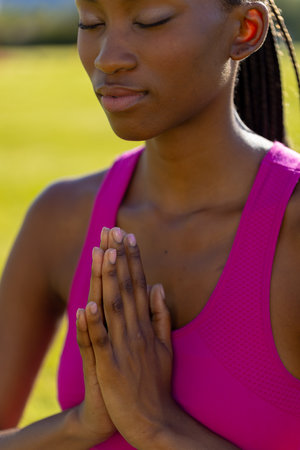 African american woman sitting on grass, doing yoga and meditating in garden. Sport, healthy and active lifestyle, summer, sunshine, unaltered.の写真素材