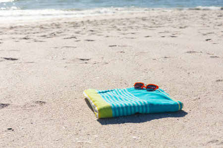 Red sunglasses on green and blue striped towel on sunny sand beach by the sea, copy space. Summer, sun, free time, relaxation and beach vacation.の写真素材