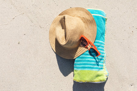 Overhead view of red sunglasses, sunhat and rolled beach towel on sunny sand beach. Summer, sun, free time, relaxation and beach vacation.の写真素材