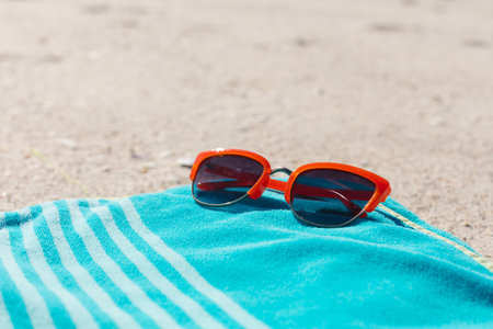 Red sunglasses on blue striped towel on sunny sand beach, copy space. Summer, sun, free time, relaxation and beach vacation.の写真素材