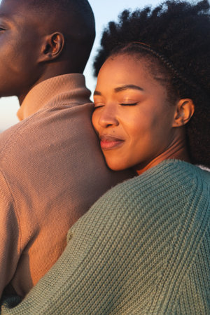 Happy african american couple embracing and smiling on sunny beach. Summer, togetherness, romance and vacation, unaltered.の写真素材
