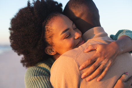Happy african american couple embracing and smiling on sunny beach. Summer, togetherness, romance and vacation, unaltered.の写真素材