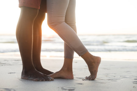 Low section of african american couple embracing on beach at sunset. Summer, togetherness, romance and vacation, unaltered.の写真素材