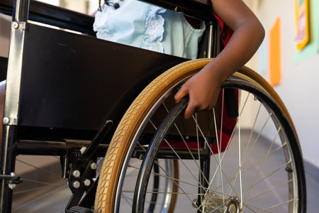 Mid section of african american schoolgirl sitting in wheelchair at elementary school corridor. Disability, education, childhood, development, learning and school, unaltered.の写真素材
