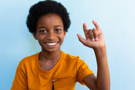 Portrait of happy biracial schoolboy doing gestures with hand over blue background. Education,...