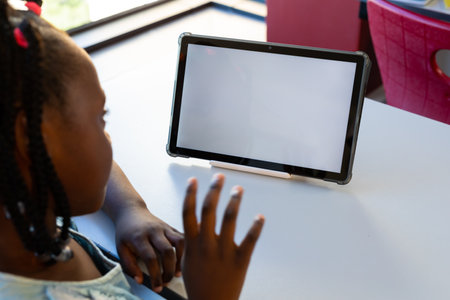 Focused african american schoolgirl using tablet with copy space at elementary school. Technology, education, childhood, development, learning and school, unaltered.の写真素材