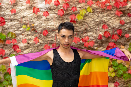 Portrait of biracial transgender man holding rainbow flag, with rocks and leaves in background. Gender, lgbtq, pride and lifestyle, unaltered.の写真素材