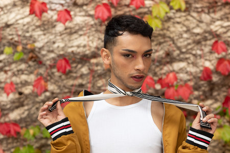 Portrait of biracial transgender man looking at camera, with rocks and leaves in background. Gender,...