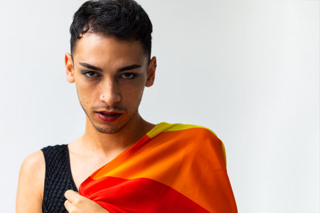 Portrait of biracial transgender man holding rainbow flag on white background, copy space. Gender, lgbtq, pride and lifestyle, unaltered.の写真素材