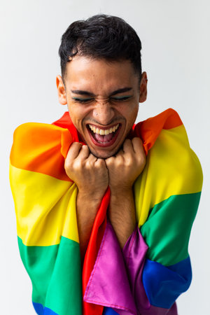 Happy biracial transgender man holding rainbow flag with eyes closed on white background. Gender, lgbtq, pride and lifestyle, unaltered.の写真素材