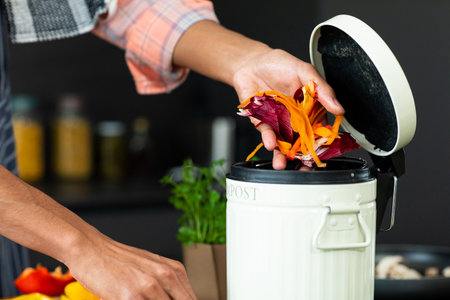 Midsection of biracial man wearing apron preparing meal, composting vegetable waste in kitchen....