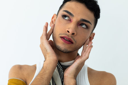 Thoughtful biracial transgender man looking away and touching face on white background. Gender,...