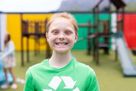 Portrait of smiling caucasian schoolgirl wearing recycling t shirt in schoolyard, with copy space. Education, inclusivity, elementary school and learning concept.の写真素材