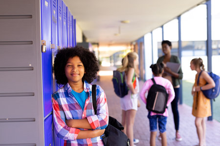Portrait of smiling biracial school girl leaning on lockers in school corridor with copy space. Education, inclusivity, elementary school and learning concept.の写真素材